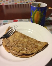 Photo of an omelet with a banana peanut butter filling on a white plate with a coffee cup