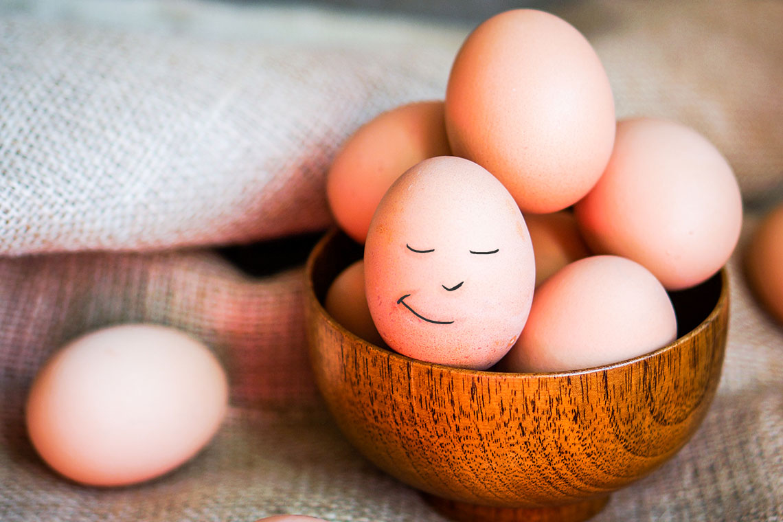 Picture of brown eggs in a basket. One egg has a drawn-on face with a grin.